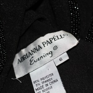 Pode incluir: Uma etiqueta branca com texto preto que diz "ADRIANNA PAPELL Evening" e "95% POLYESTER 5% SPANDEX MADE IN CHINA OFF REVERSE DE" com uma etiqueta de tamanho 6 anexada.