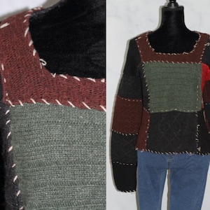 Op de afbeelding: Een zwarte, bruine, groene en rode patchworktrui met witte stiksels. De trui heeft een ronde hals en lange mouwen.