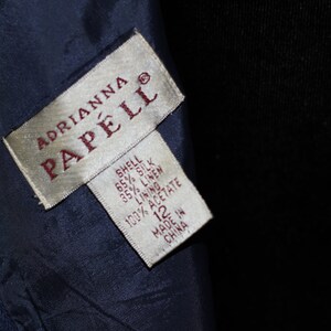 May include: A white tag with the text "ADRIANNA PAPELL" in red lettering. The tag also includes the fabric composition: "SHELL 65% SILK 35% LINEN LINING 100% ACETATE" and the size "12". The tag is made in China.
