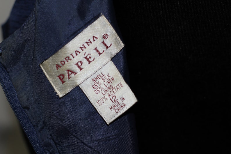 May include: A white tag with the text "ADRIANNA PAPELL" in red lettering. The tag also includes the fabric composition: "SHELL 65% SILK 35% LINEN LINING 100% ACETATE" and the size "12". The tag is made in China.