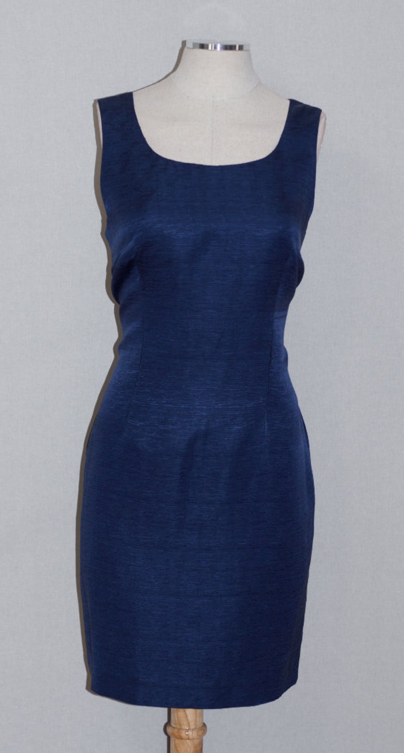 May include: A sleeveless, navy blue dress with a square neckline. The dress is made of a textured fabric and has a fitted silhouette.
