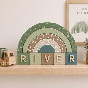 May include: A wooden rainbow toy in shades of green, brown, and blue, adorned with stars and dots. The word "RIVER" is spelt out with individual wooden blocks. A wooden toy truck and a framed print are also visible.