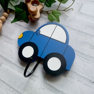 May include: A blue wooden car shaped hook with black tyres and a white windscreen. The hook is attached to a white wall.