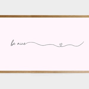 Könnte beinhalten: Ein gerahmter Druck mit rosa Hintergrund und schwarzem Text, der "be mine" lautet, mit einem kleinen Herz, das in einer durchgehenden Linie gezeichnet ist.