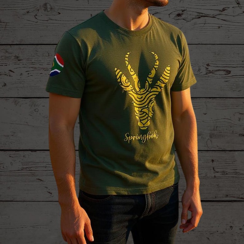 Puede incluir: Camiseta verde oliva con un dise&ntilde;o de springbok amarillo y la palabra "Springbok". La bandera sudafricana est&aacute; en la manga izquierda. La camiseta se combina con vaqueros azul oscuro.