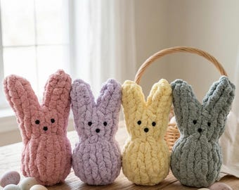 May include: Four handmade, plush bunny figures in pink, lavender, yellow, and gray, with black button eyes. The bunnies are arranged on a wooden surface with decorative Easter eggs and a woven basket in the background. A tag reads "Handmade with Love."