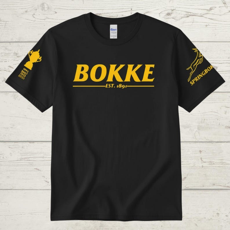 May include: Black t-shirt with gold text and graphics. The word "BOKKE" is centered, with "EST. 1891" below. A trophy graphic and the years 1995, 2007, 2019, and 2023 are on the left sleeve. The right sleeve has a Springbok logo.