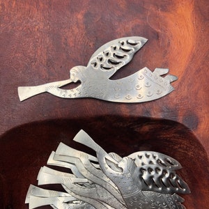 May include: A set of 10 silver metal angel ornaments with intricate cut-out designs. The angels are holding trumpets and have wings with a repeating pattern of circles and stars.