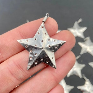 May include: Silver metal star ornament with a spring loop for hanging. The star has a textured surface with small holes throughout.