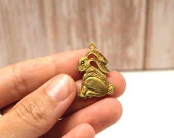 May include: A gold-colored metal charm in the shape of a rabbit. The rabbit is sitting with its ears up and its tail behind it.