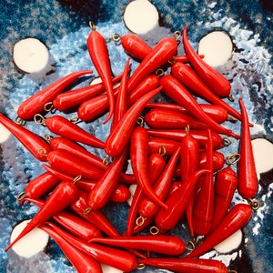 May include: A pile of bright red, pointed glass beads with gold metal loops. The beads are arranged in a bowl with a blue and white polka dot pattern.