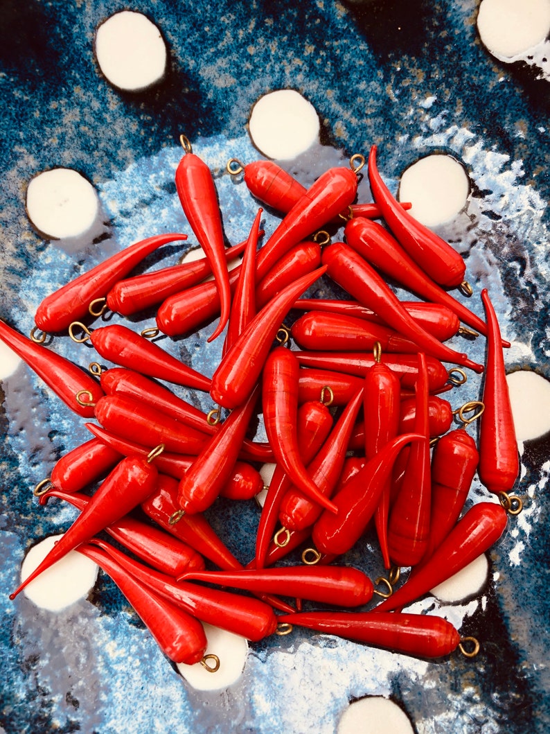 May include: A pile of bright red, pointed glass beads with gold metal loops. The beads are arranged in a bowl with a blue and white polka dot pattern.