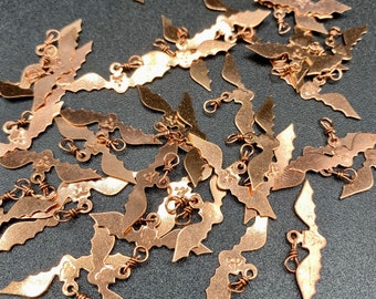 May include: A pile of copper-colored metal bat charms with a loop for hanging. The charms are in the shape of a bat with wings spread out.