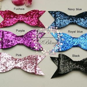 May include: Ten glitter hair bows in various colours, including fuchsia, purple, pink, navy blue, royal blue, and black. The bows are arranged in two rows of five.