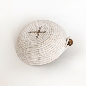 May include: A white woven bowl with a brown cross design and a wooden handle.