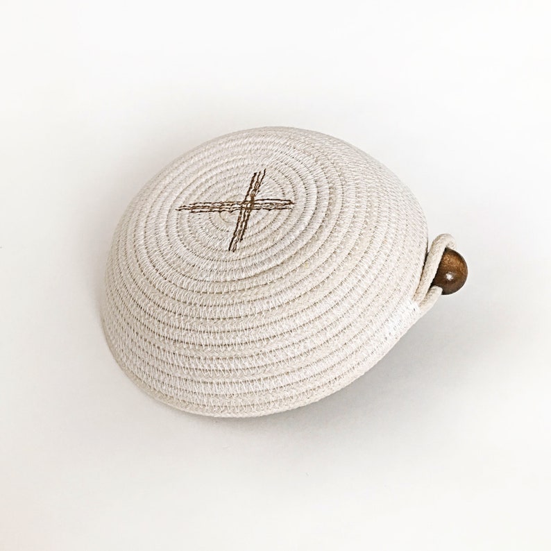 May include: A white woven bowl with a brown cross design and a wooden handle.