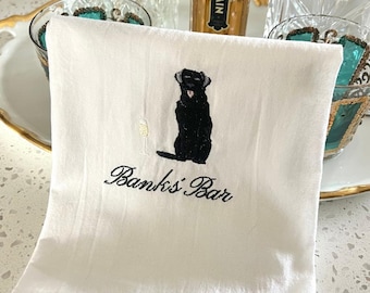 Può includere: Asciugamano da bar in cotone bianco con un ricamo nero di un Labrador Retriever con un bicchiere di champagne. Il testo "Banks' Bar" è ricamato sotto. L'asciugamano è piegato.