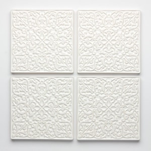 Könnte beinhalten: Vier quadratische, weiße Keramikuntersetzer mit einem erhabenen, verzierten Blumen- und Rankenmuster. Die Untersetzer sind quadratisch angeordnet und zeigen das detaillierte, symmetrische Muster. Das Design ist auf allen vier Teilen identisch.