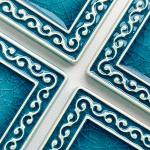 Può includere: Primo piano di quattro piastrelle quadrate in ceramica. Ogni piastrella è di colore verde acqua intenso con una glassa craquelé e un bordo bianco ornato. Il bordo presenta un motivo a volute ripetuto. Le piastrelle sono disposte a formare un quadrato più grande.