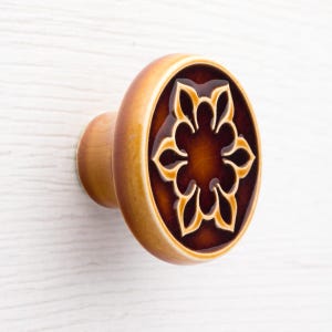 Op de afbeelding: Een decoratieve kastknop met een bloemmotief. De knop heeft een bruin en beige kleurenschema met een glanzende afwerking. Het bloemmotief is gecentreerd op de voorkant van de knop.