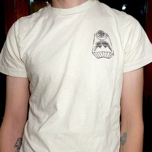 May include: A white t-shirt with a black and white graphic of a monster with one eye on the front.