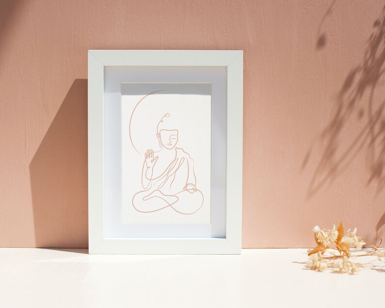 Puede incluir: Un marco blanco con un dibujo de l&iacute;nea de un Buda meditando en posici&oacute;n sentada. El dibujo es de color marr&oacute;n claro.