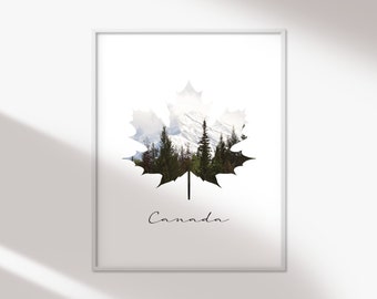 May include: A white framed print with a black silhouette of a maple leaf. The leaf is filled with a photo of a snowy mountain range and pine trees. The text "Canada" is written in cursive below the leaf.