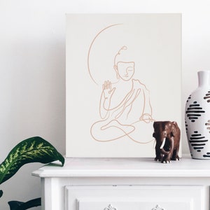 Puede incluir: Un dibujo de l&iacute;nea de un Buda meditando en un lienzo blanco con una figurita de elefante de madera marr&oacute;n y un jarr&oacute;n de cer&aacute;mica blanco con patrones geom&eacute;tricos negros en un estante blanco.