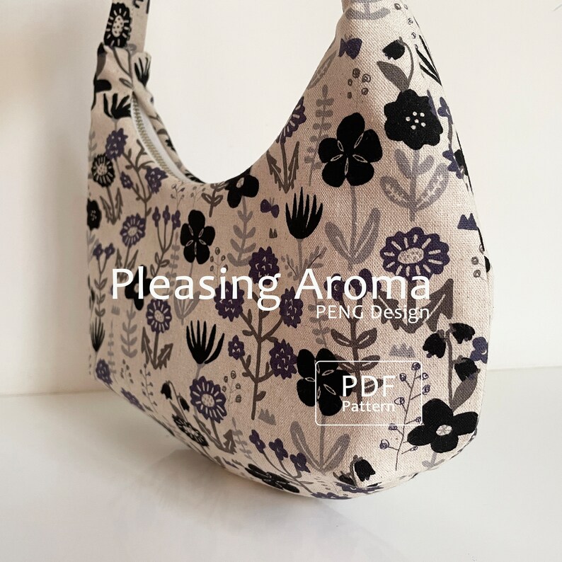 May include: A white fabric tote bag with a black and grey floral pattern. The bag has a curved shape and a zipper closure. The text "Pleasing Aroma PENG Design PDF Pattern" is printed on the bag.