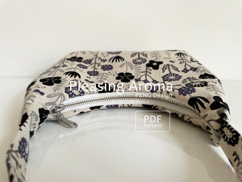 May include: A beige fabric bag with a black and purple floral print and a silver zipper. The bag has a strap and the text "Pleasing Aroma PENG Design" is printed on the front. The text "PDF Pattern" is printed on a white rectangle.