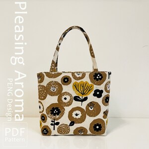 Op de afbeelding: Een witte tote bag met een bloemenpatroon in tinten bruin, geel en zwart. De tas heeft een bruin stoffen handvat en de tekst "Pleasing Aroma PDF Pattern" is afgedrukt aan de linkerkant van de afbeelding.