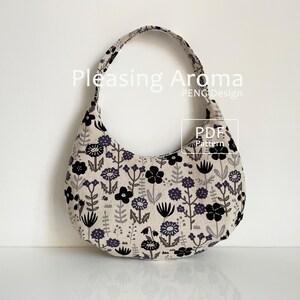 May include: A black and white floral print fabric tote bag with a curved shape and a single strap. The bag is made of a soft, natural fabric and has a simple, elegant design. The text "Pleasing Aroma PENG Design PDF Pattern" is visible on the bag.