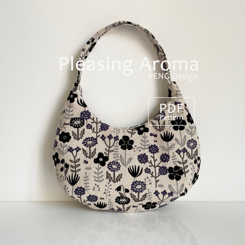 May include: A black and white floral print fabric tote bag with a curved shape and a single strap. The bag is made of a soft, natural fabric and has a simple, elegant design. The text "Pleasing Aroma PENG Design PDF Pattern" is visible on the bag.