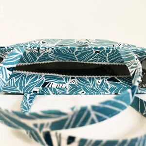 Op de afbeelding: Een teal en witte tote bag met een ritssluiting en een bladmotief. De tas is open en de binnenkant is zichtbaar.