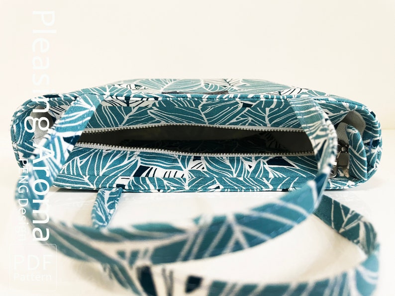 Op de afbeelding: Een teal en witte tote bag met een ritssluiting en een bladmotief. De tas is open en de binnenkant is zichtbaar.