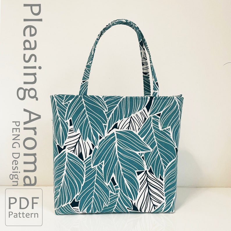 Op de afbeelding: Een teal-kleurige tote bag met een wit en zwart bladmotief. De tas heeft twee handvatten en is gemaakt van stof. De tekst "Pleasing Aroma PENG Design PDF Pattern" is gedrukt aan de linkerkant van de afbeelding.