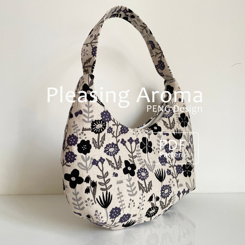 May include: A beige fabric handbag with a black floral print and a zipper closure. The bag has a single strap and is shaped like a crescent moon. The text "Pleasing Aroma PENG Design PDF Pattern" is visible on the bag.