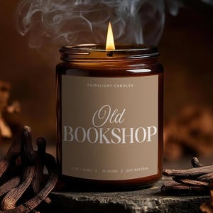 Könnte beinhalten: Eine brennende Kerze in einem braunen Glas mit der Aufschrift "Old Bookshop". Rauch steigt von der Flamme auf. Die Kerze ist von getrockneten Pflanzen umgeben. Die Kerze ist 255g und 100% natürlich.