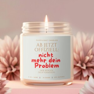 Könnte beinhalten: Eine Kerze im klaren Glasgefäß mit einem weißen Etikett, das den Text "FAIRYLIGHT CANDLES AB JETZT OFFIZIELL: nicht mehr dein Problem (WIR WERDEN DICH VERMISSEN) 9 OZ / 255G | 50 HOURS | 100% NATURAL" in schwarzer und roter Schrift trägt, mit brennendem Docht.