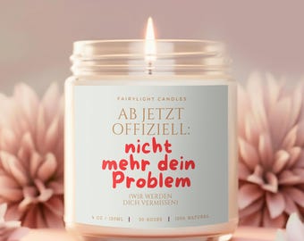 May include: A clear glass jar candle with a white label featuring the text "FAIRYLIGHT CANDLES AB JETZT OFFIZIELL: nicht mehr dein Problem (WIR WERDEN DICH VERMISSEN) 9 OZ / 255G | 50 HOURS | 100% NATURAL" in black and red lettering with a lit wick.