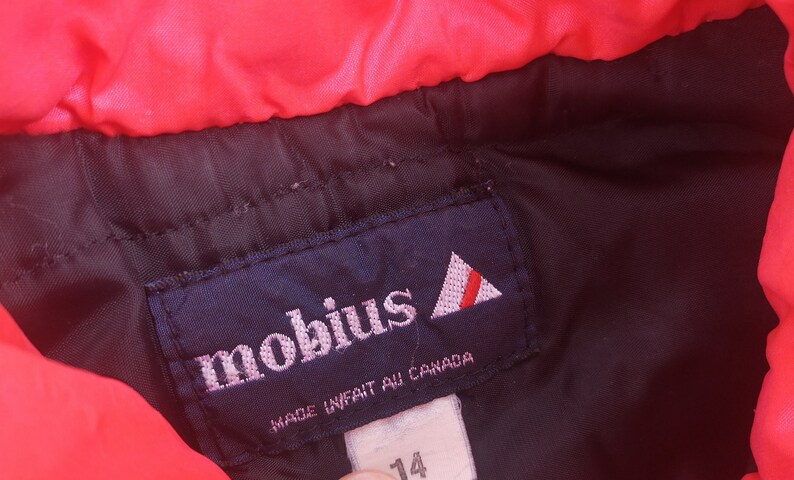 Pode incluir: Um r&oacute;tulo azul com a palavra "mobius" em letras brancas e um logotipo triangular vermelho e branco. O r&oacute;tulo tamb&eacute;m diz "Made in/fait au Canada".