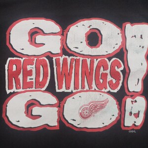 May include: A black t-shirt with a white and red graphic that says "Go Red Wings Go!" with a red winged hockey logo in the centre.