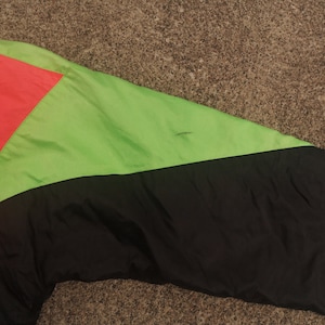 Pode incluir: Uma jaqueta preta, verde e rosa com fecho de correr. A jaqueta &eacute; feita de nylon e tem um design desportivo.