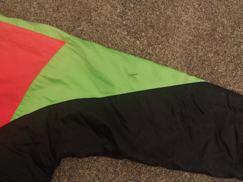 Pode incluir: Uma jaqueta preta, verde e rosa com fecho de correr. A jaqueta &eacute; feita de nylon e tem um design desportivo.
