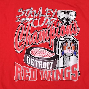 May include: Red t-shirt featuring a graphic of the Detroit Red Wings 1997 Stanley Cup Championship. The graphic includes the Stanley Cup trophy, a hockey puck, and the team's logo.