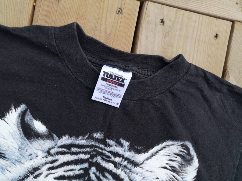 Może przedstawiać: Czarny T-shirt z białym nadrukiem zebry. Koszulka ma metkę Tultex z napisem "Preshrunk 100% Cotton" i "Medium/Moyen/M".