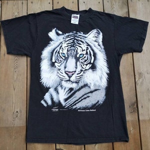 Może przedstawiać: Czarny T-shirt z grafiką białego tygrysa i tekstem "African Lion Safari".