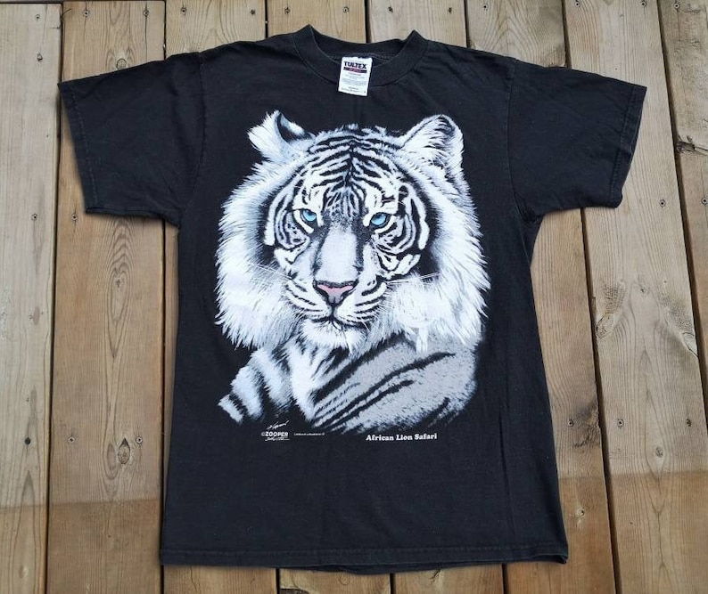 Może przedstawiać: Czarny T-shirt z grafiką białego tygrysa i tekstem "African Lion Safari".