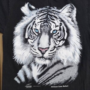 Może przedstawiać: Czarny T-shirt z grafiką białego tygrysa i tekstem "African Lion Safari".