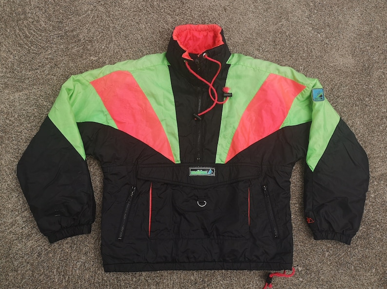 Pode incluir: Uma jaqueta de esqui vintage preta, verde e rosa com fecho de z&iacute;per at&eacute; a metade e um pequeno logotipo na manga superior direita. A jaqueta tem um bolso grande na frente com um cord&atilde;o.